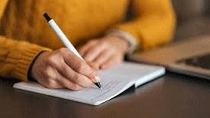A woman writing in a notebook with a pen.