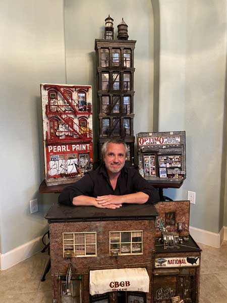 A man posing in front of a collection of toy buildings.
