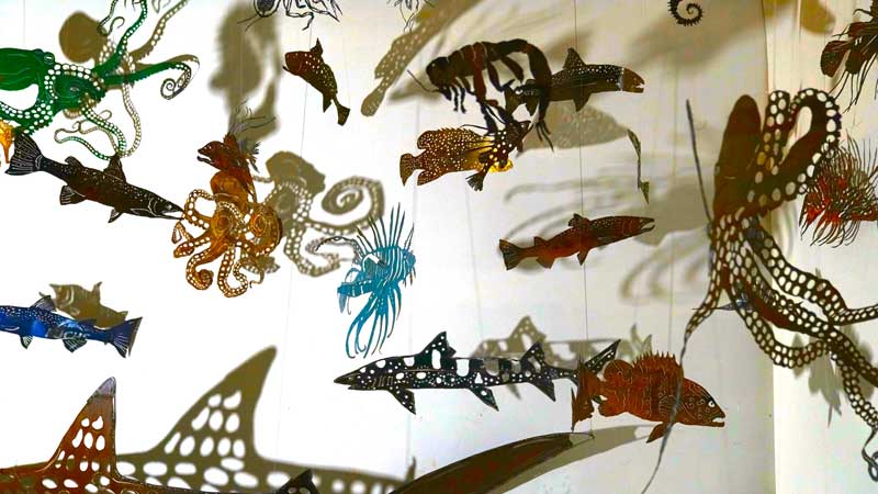 A group of metal fish sculptures hanging on a wall.